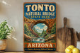 A vintage-style sign for Tonto Natural Bridge State Park in Arizona, featuring an illustration of the arch and a waterfall.