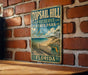 A vintage metal sign for Top sail Hill Preserve State Park in Florida, featuring a beach scene and palm trees, is displayed on a brick wall.