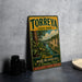 A vintage-style sign for Torreya State Park, featuring a scenic illustration of a river and lush vegetation, placed on a gray countertop next to a stack of black camera lenses.