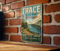 A vintage metal sign for Trace State Park in Mississippi, featuring a scenic landscape with a river and trees.