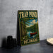 A vintage metal sign for Trap Pond State Park in Delaware, featuring an illustration of a red canoe on a lake surrounded by trees and a cloudy sky.