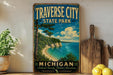 A vintage-style sign for Traverse City State Park in Michigan, featuring a scenic coastal landscape with a beach, cliffs, and a lake.