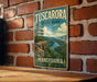 A vintage-style metal sign for Tuscarora State Park in Pennsylvania, featuring a scenic landscape with a river and mountains.