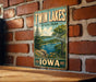 A vintage-style metal sign for Twin Lakes State Park in Iowa, featuring a scenic landscape with a lake, trees, and a sailboat.