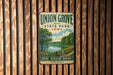 A vintage metal sign for Union Grove State Park in Iowa, featuring a scenic landscape with a lake, trees, and a path.
