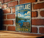 A vintage-style metal sign for the Unity Lake State Recreation Site in Oregon, featuring a scenic landscape with a lake, mountains, and pine trees.