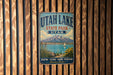 A vintage metal sign for Utah Lake State Park, featuring a scenic mountain landscape with a lake and a sailboat.