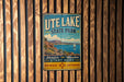 A vintage metal sign for Utah Lake State Park, featuring a scenic illustration of the lake and mountains, hangs on a wooden wall.