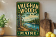 A vintage-style sign for Vaughan Woods State Park in Maine, featuring a scenic landscape with a river, trees, and a wooden fence.