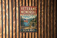 A vintage metal sign for the Veterans Memorial State Park in Idaho, featuring an American flag and a scenic landscape.