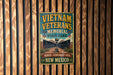 a vintage-style metal sign with the text "Vietnam Veterans Memorial State Park" and "Honor + Remember + Heal New Mexico" displayed on a wooden wall.