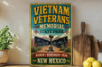 a vintage-style sign for the Vietnam Veterans Memorial in New Mexico, with a wooden board and a potted plant in the background.