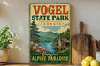 A vintage-style sign for Vogel State Park in Georgia, featuring a scenic mountain landscape with a cabin and flowers.
