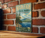 A vintage-style metal sign for Wadleigh State Park in New Hampshire, featuring a scenic landscape with a lake, mountains, and pine trees.