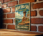 A vintage-style metal sign for Wah-Sha-She State Park in Oklahoma, featuring a scenic landscape with a rock formation and a lake.