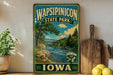 A vintage-style metal sign for Wapsipenic State Park in Iowa, featuring a scenic landscape with a river, bridge, and trees.