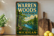 A vintage-style sign for Warren Woods State Park in Michigan, featuring a scenic illustration of a forest and a river.