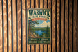 A vintage metal sign for Warwick State Forest in Massachusetts, featuring a scenic image of a lake surrounded by pine trees and mountains.