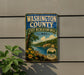 A vintage-style metal sign for Washington County, Illinois, featuring a scenic landscape with a river, trees, and flowers.