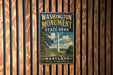 A vintage-style metal sign for Washington Monument State Park in Maryland, featuring a scenic image of the monument surrounded by trees and a lake.
