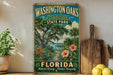 A vintage-style sign for Washington Oaks Gardens State Park in Florida, featuring a tropical landscape with palm trees, flowers, and a path leading to the park.