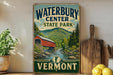 A vintage-style sign for Waterbury Center State Park in Vermont, featuring a red wooden bridge over a river surrounded by mountains and pine trees.