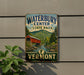 A vintage-style sign for Waterbury Center State Park in Vermont, featuring a red wooden bridge and a scenic mountain landscape.