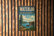 A vintage metal sign for the Waterloo Recreation Area in Michigan, featuring a scenic illustration of a lake, pine trees, and a red canoe.
