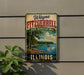 A vintage-style metal sign for the Illinois State Recreation Area, featuring a scenic landscape with a lake, trees, and a boat.