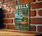 A vintage metal sign for Wells State Park in Massachusetts, featuring a scenic landscape with a lake and trees.