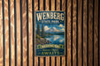 A vintage-style metal sign for Wenberg State Park, featuring a scenic mountain landscape with pine trees and a lake.