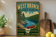 A vintage-style sign for West Branch State Park, featuring a scenic image of a lake and forest, with a red canoe on the shore.