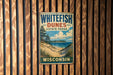 A vintage metal sign for Whitefish Dunes State Park in Wisconsin, featuring a scenic landscape with a beach, dunes, and a lake.