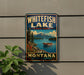 A vintage-style metal sign for Whitefish Lake State Park in Montana, featuring a scenic landscape with mountains, a lake, and a boat.