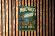 A vintage metal sign for Wildwood State Park in New York, featuring a scenic landscape with a lake, mountains, and pine trees.