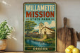 A vintage-style poster of Willamette Mission State Park in Oregon, featuring a scenic illustration of a church and a stream, is displayed on a wall next to a wooden cutting board and some potted plants.