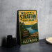 A vintage metal sign for William G. Stratton State Park in Illinois, featuring a scenic landscape with a lake and mountains.