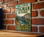 A vintage-style metal sign for William M. Tugman State Park in Oregon, featuring a scenic mountain landscape with a river and pine trees.