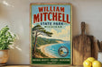 A vintage-style metal sign for William Mitchell State Park in Michigan, featuring a scenic landscape with a pine tree, beach, and ocean.