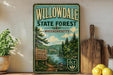 a vintage-style sign for Willowdale State Forest in Massachusetts, with a scenic illustration of a forest and a river. The sign is displayed on a shelf next to a wooden cutting board and a potted plant.
