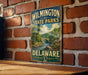 A vintage metal sign for Wilmington State Parks in Delaware, featuring a scenic landscape with a river and bridge.