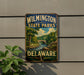 A vintage metal sign for Wilmington State Parks in Delaware, featuring a scenic landscape with a river and bridge.