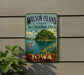 A vintage-style metal sign for Wilson Island, Iowa, featuring a scenic landscape with a lake, a bird, and flowers.