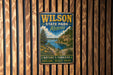 A vintage metal sign for Wilson State Park in Kansas, featuring a scenic landscape with a river, mountains, and trees.