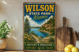A vintage-style metal sign for Wilson State Park in Kansas, featuring a scenic landscape with a river, mountains, and a path leading through the greenery.