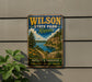 A vintage-style metal sign for Wilson State Park in Kansas, featuring a scenic landscape with a river, mountains, and a path leading through the natural setting.