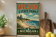 A vintage-style metal sign for Wilson State Park in Michigan, featuring a scenic landscape with pine trees, a beach, and a lake.