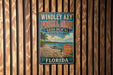 A vintage-style metal sign for Windley Key Fossil Reef, Florida State Park, featuring a beach scene and palm trees.