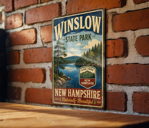 A vintage-style metal sign for Winslow State Park in New Hampshire, featuring a scenic landscape with pine trees, a lake, and mountains.