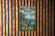 A vintage metal sign for Wolf's Neck Woods State Park in Maine, featuring a scenic landscape with pine trees, a lake, and a bird in flight.
